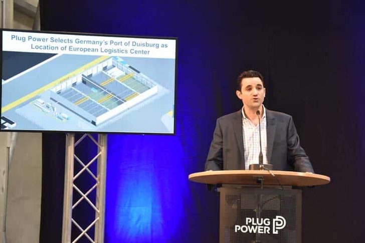 Man speaking at a podium with Plug Power logo; screen shows announcement about Port of Duisburg logistics center. Man speaking at a podium with Plug Power logo; screen shows announcement about Port of Duisburg logistics center.