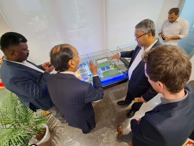 Four men in suits discuss over a detailed architectural model table; another man stands in the background. Four men in suits discuss over a detailed architectural model table; another man stands in the background.