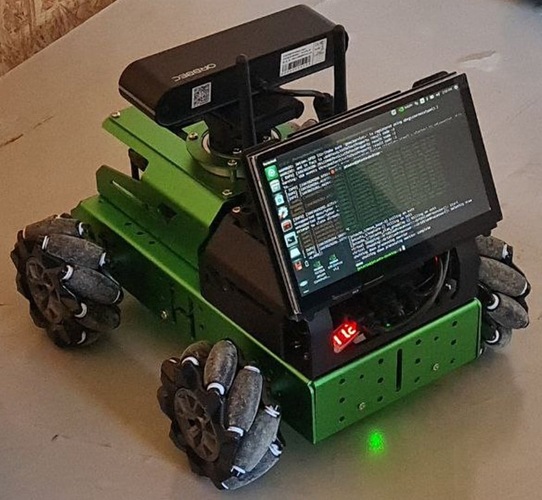 A green robotic vehicle with omni wheels and a mounted screen displaying code or terminal output. A green robotic vehicle with omni wheels and a mounted screen displaying code or terminal output.