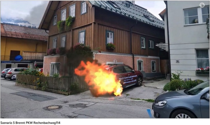 A car parked by a house is on fire, with flames and smoke coming from its front end. A car parked by a house is on fire, with flames and smoke coming from its front end.