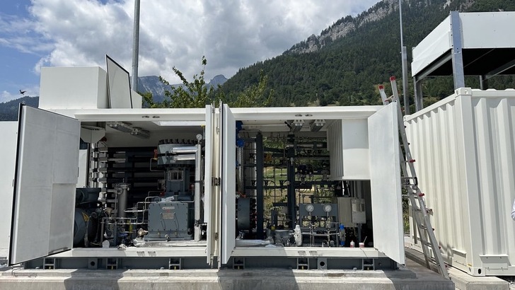 Two open industrial equipment containers with machinery, set outdoors near mountains and trees under a cloudy sky.