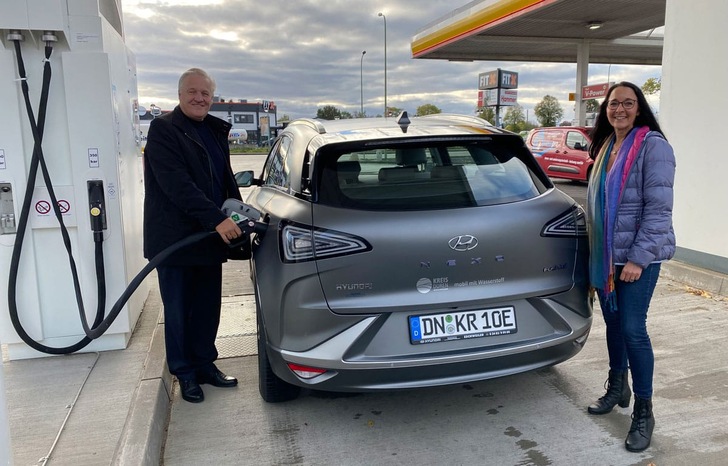 Two people refueling a silver Hyundai at a gas station, with a Shell sign visible in the background. Two people refueling a silver Hyundai at a gas station, with a Shell sign visible in the background.