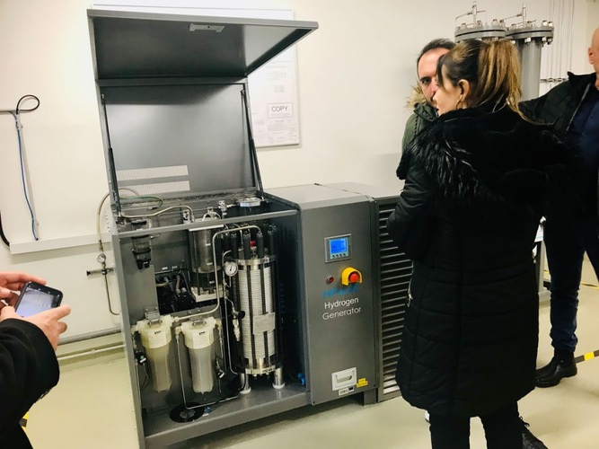 People examine a hydrogen generator machine displayed in a laboratory setting. People examine a hydrogen generator machine displayed in a laboratory setting.