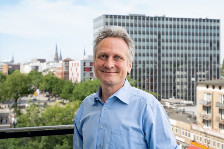 Smiling man in a blue shirt standing on a balcony with city buildings and trees in the background. Smiling man in a blue shirt standing on a balcony with city buildings and trees in the background.