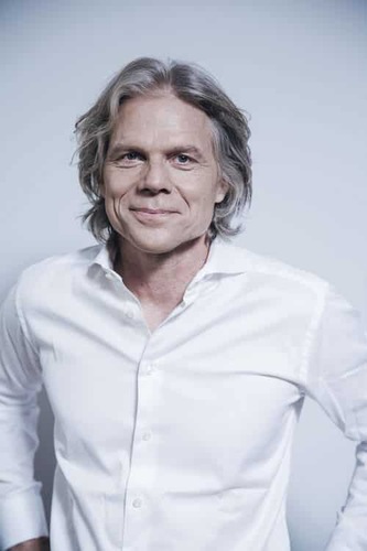 Middle-aged man with gray hair smiles, wearing a white button-up shirt against a plain light background. Middle-aged man with gray hair smiles, wearing a white button-up shirt against a plain light background.