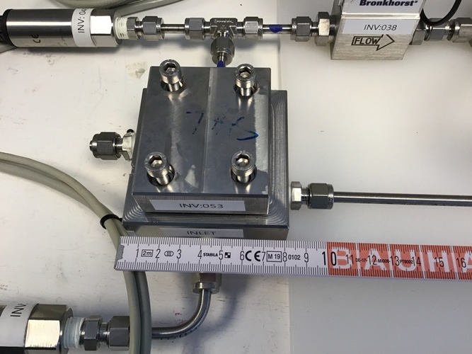 Metal flow control device with labeled pipes and a ruler showing measurements in centimeters and millimeters.