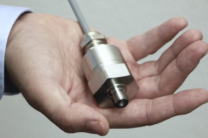 A hand holding a metal industrial sensor with a cable attached. A hand holding a metal industrial sensor with a cable attached.