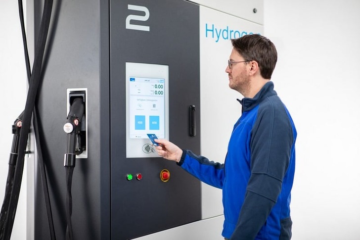 Man using a touchscreen at a hydrogen fuel station, holding a card near the payment terminal. Man using a touchscreen at a hydrogen fuel station, holding a card near the payment terminal.
