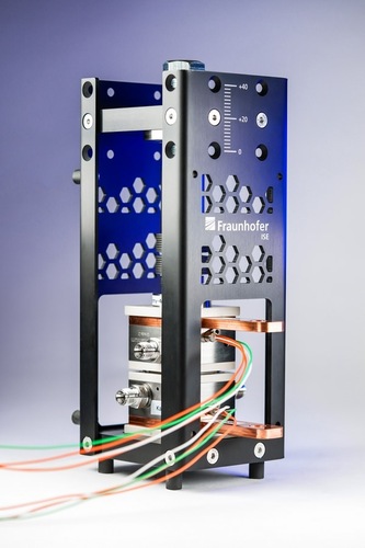A metallic scientific instrument with wires and Fraunhofer ISE logo, against a light background. A metallic scientific instrument with wires and Fraunhofer ISE logo, against a light background.