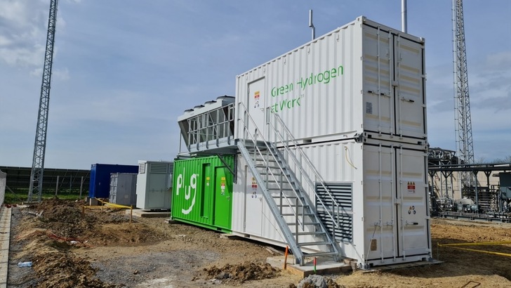 Two stacked containers labeled "Green Hydrogen Network" at an industrial site, with stairs and equipment nearby. Two stacked containers labeled "Green Hydrogen Network" at an industrial site, with stairs and equipment nearby.