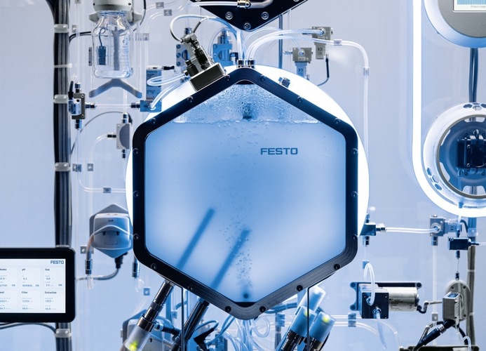 Hexagonal device labeled "FESTO" with tubes and wires, part of a futuristic laboratory setup. Hexagonal device labeled "FESTO" with tubes and wires, part of a futuristic laboratory setup.