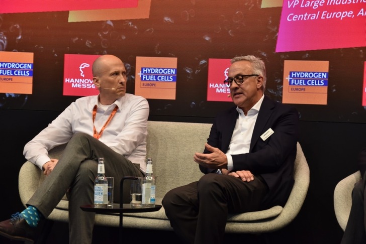Two men in business attire sit on stage discussing at the Hydrogen Fuel Cells Europe event, Hannover Messe. Two men in business attire sit on stage discussing at the Hydrogen Fuel Cells Europe event, Hannover Messe.