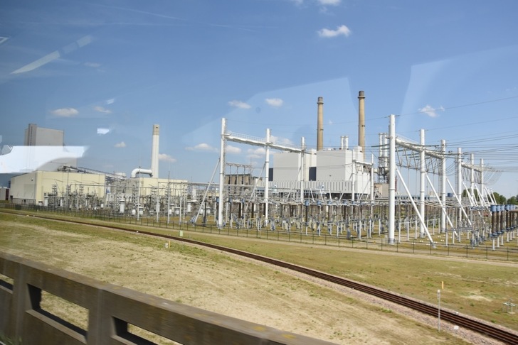 A large electrical substation with power lines, metal structures, and smokestacks under a blue sky.