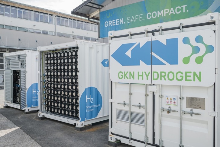 Three white GKN Hydrogen storage containers labeled H2 outside an industrial building.