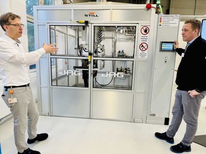 Two men discussing beside industrial machinery in a lab setting with safety signs visible on the equipment. Two men discussing beside industrial machinery in a lab setting with safety signs visible on the equipment.