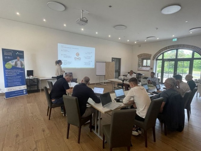 People in a conference room attend a presentation, with laptops open and a projector displaying slides. People in a conference room attend a presentation, with laptops open and a projector displaying slides.