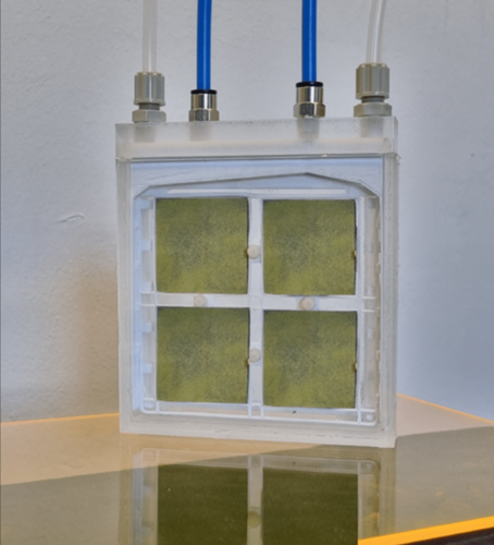 A square device with four yellow-green panels, blue and clear tubes attached at the top, on a clear surface. A square device with four yellow-green panels, blue and clear tubes attached at the top, on a clear surface.