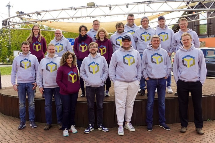 Group of people posing outdoors, wearing matching hoodies with a colorful geometric logo on the front. Group of people posing outdoors, wearing matching hoodies with a colorful geometric logo on the front.
