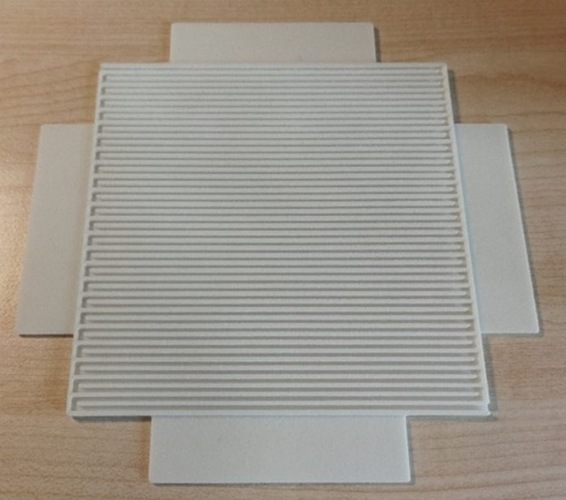 A square, grooved ceramic tile with extended edges on a wooden surface. A square, grooved ceramic tile with extended edges on a wooden surface.