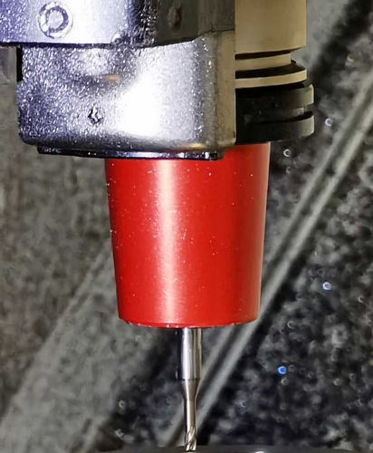 Close-up of a CNC machine spindle with a red tool holder and a cutting bit attached.