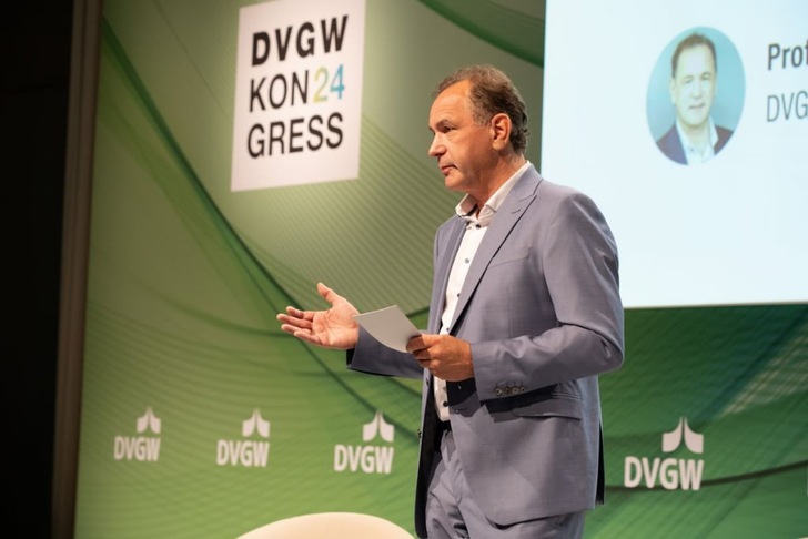 A man in a light blue suit speaks on stage at the DVGW KON24GRESS conference. A man in a light blue suit speaks on stage at the DVGW KON24GRESS conference.