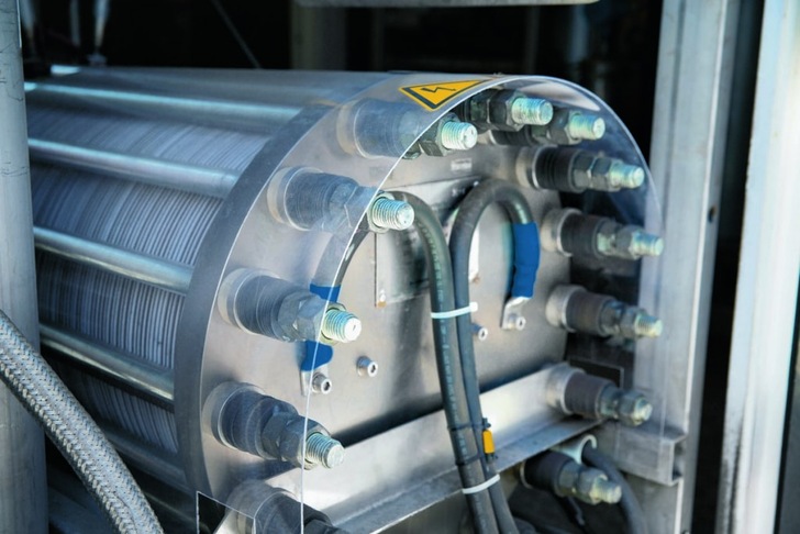 Close-up of industrial machinery with bolts, wires, and warning label, likely part of a mechanical system. Close-up of industrial machinery with bolts, wires, and warning label, likely part of a mechanical system.