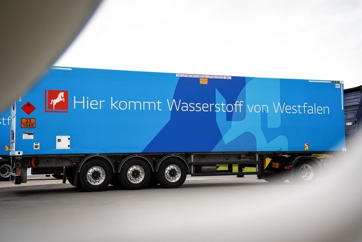 A blue truck trailer with German text: "Hier kommt Wasserstoff von Westfalen" parked on a street. A blue truck trailer with German text: "Hier kommt Wasserstoff von Westfalen" parked on a street.