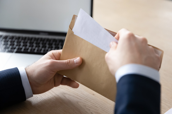 Close up back view of businessman sit at office desk open envelope with postal paper document, male employee unpack post paperwork letter or correspondence with decision notification or law order
